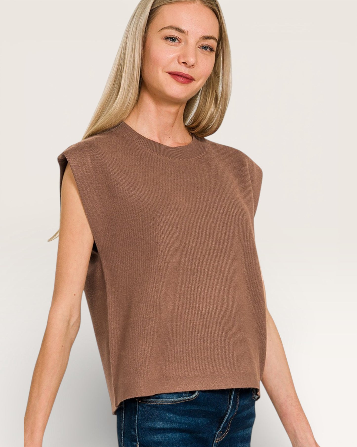 Woman wearing a brown sleeveless top against a plain background