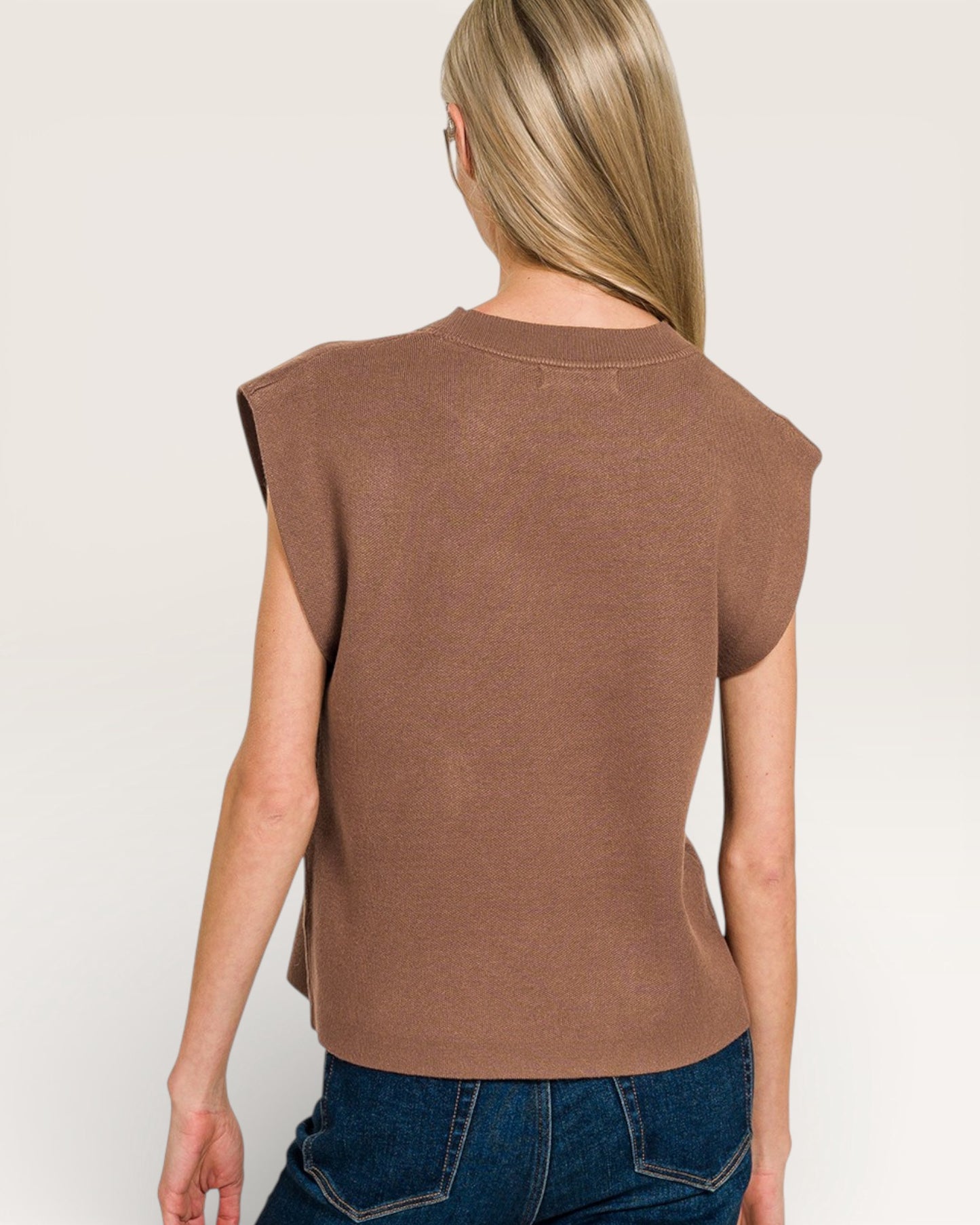 Person wearing a brown sleeveless top and blue jeans on a plain background