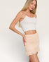 Woman wearing a white crop top and beige ruched skirt on a plain background