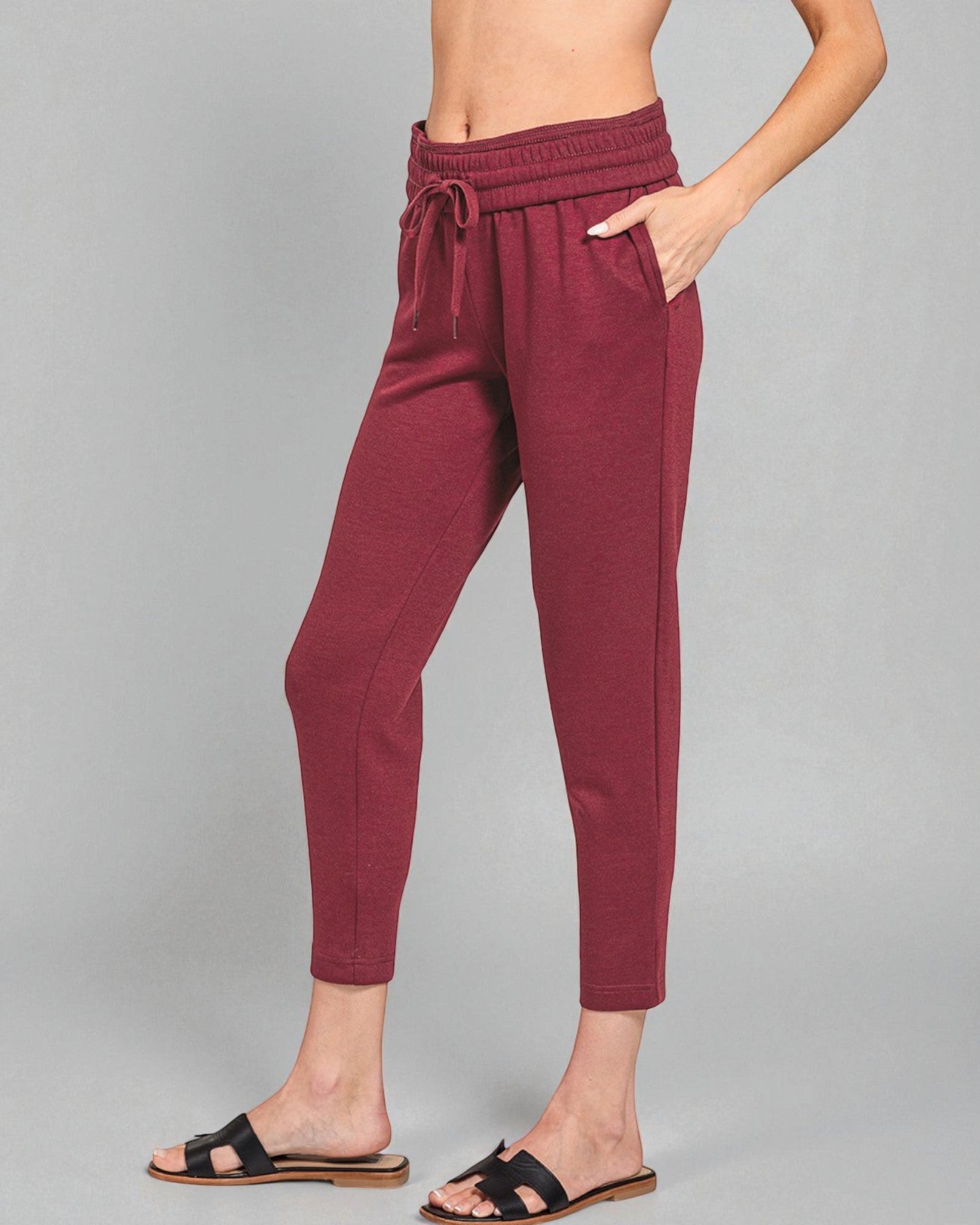 Maroon jogger pants worn by a person on a gray background