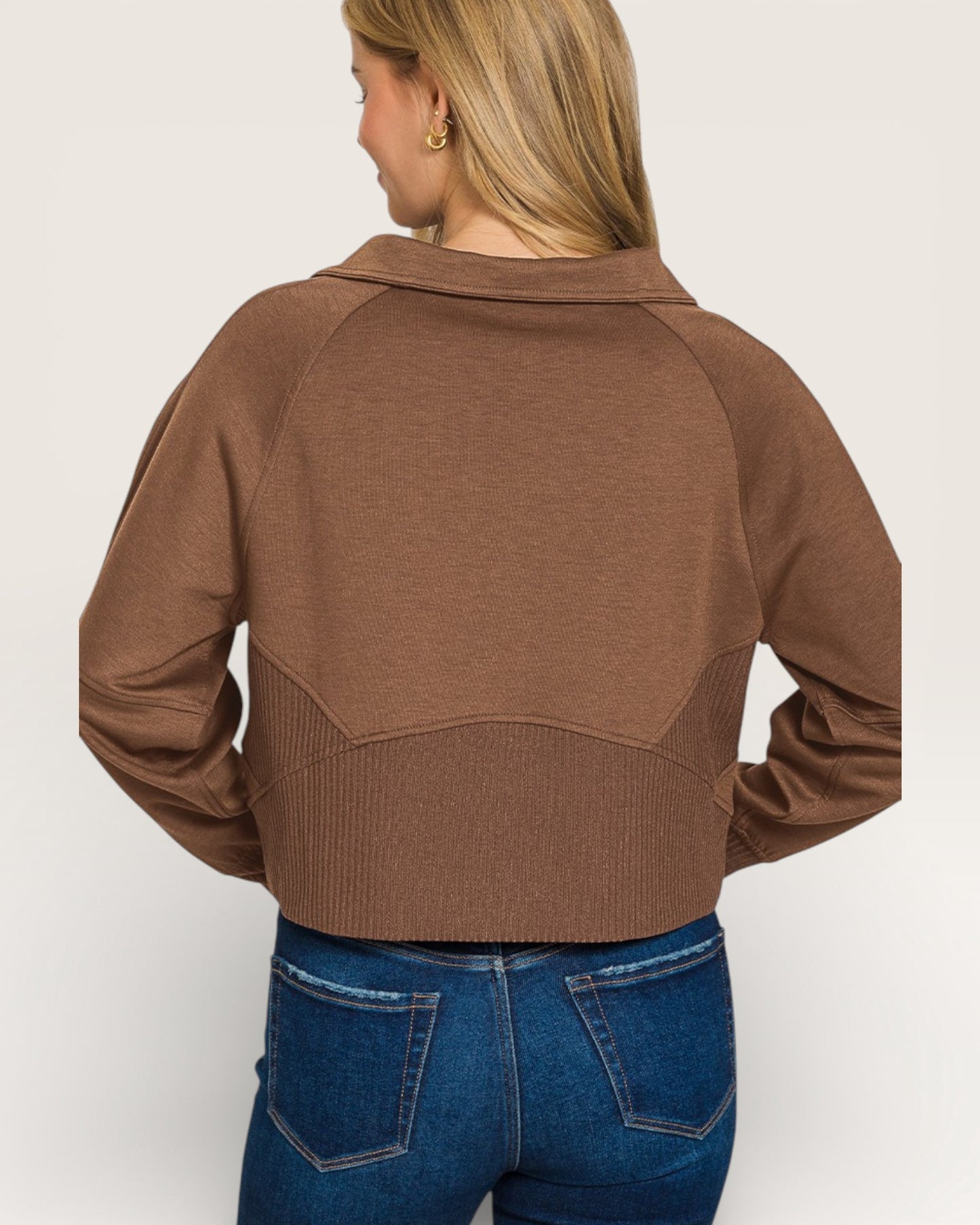 Person wearing a brown cropped jacket and blue jeans on a plain background