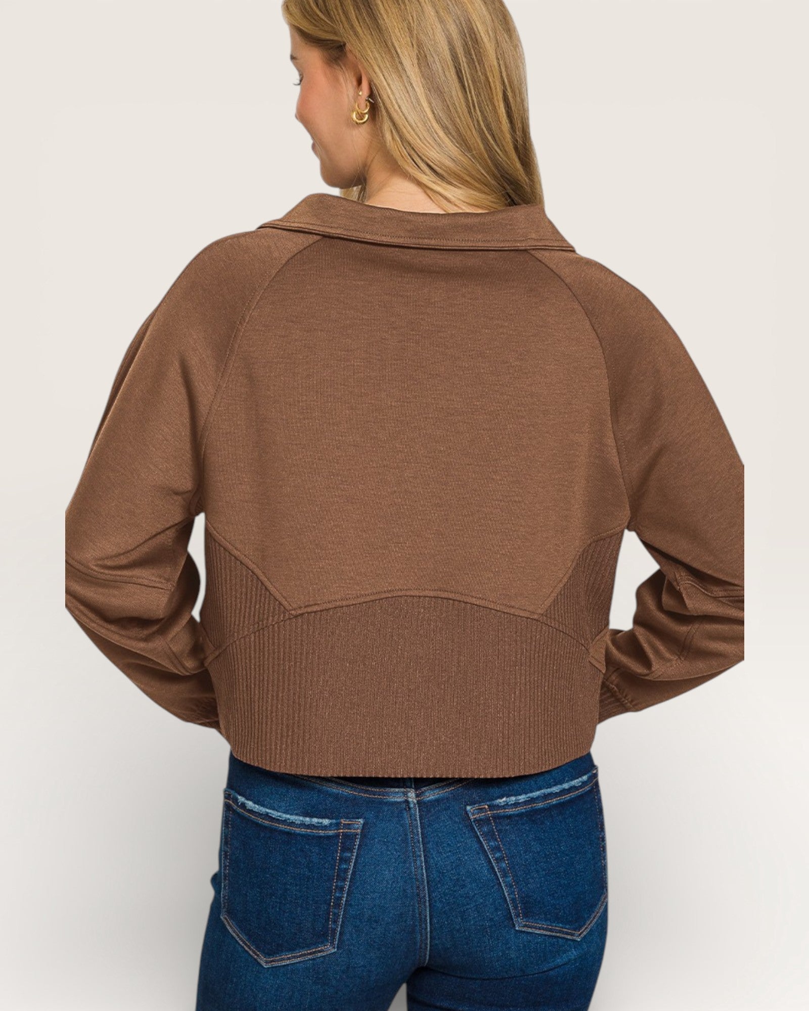 Person wearing a brown cropped jacket and blue jeans on a plain background