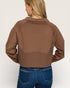 Person wearing a brown cropped jacket and blue jeans on a plain background