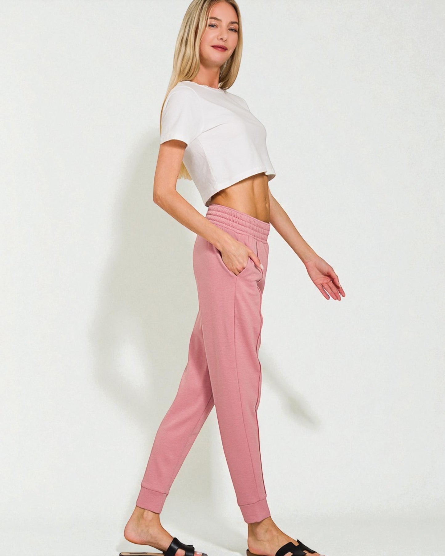 Woman wearing a white crop top and pink pants on a plain background