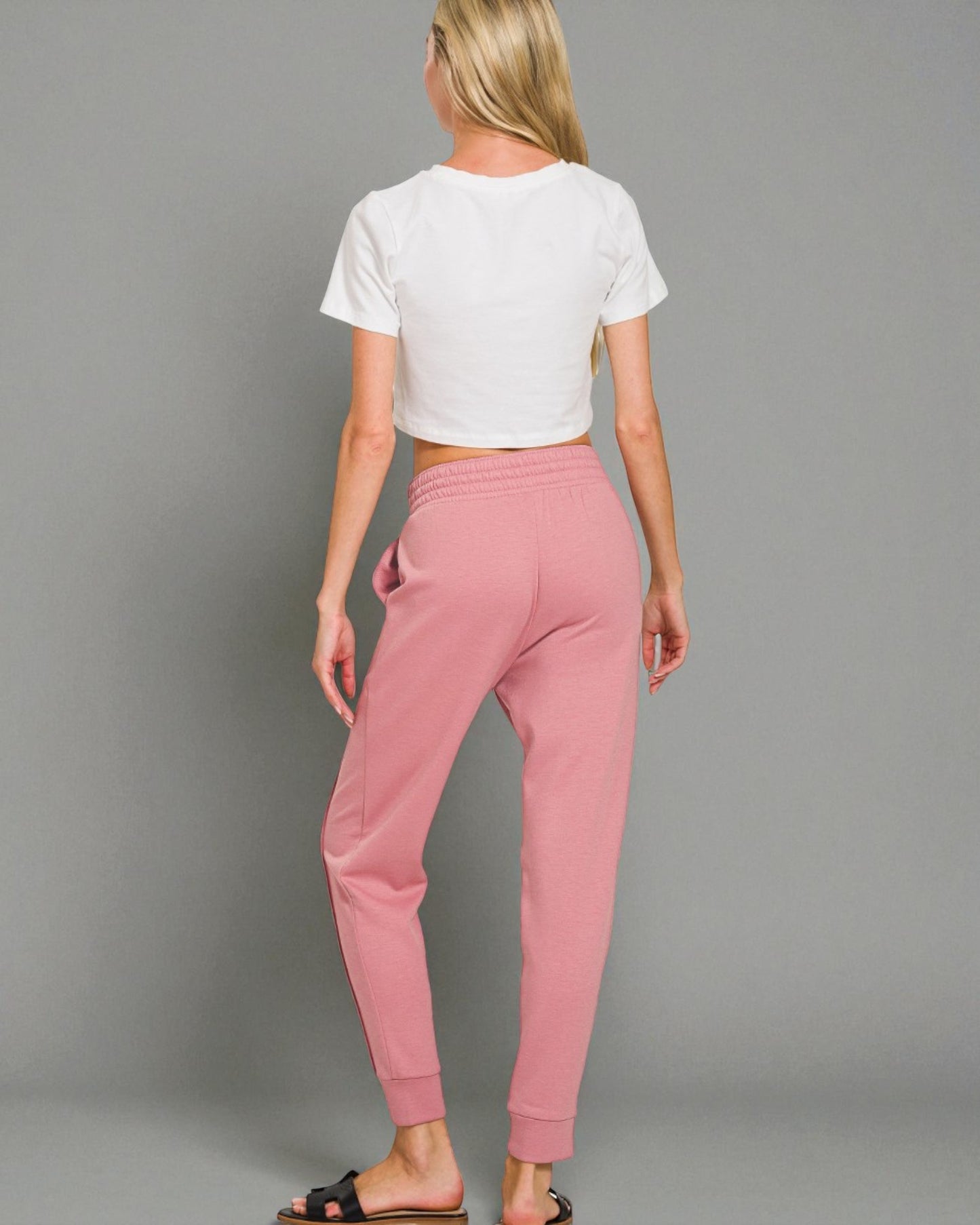 Person wearing a white crop top and pink sweatpants on a gray background