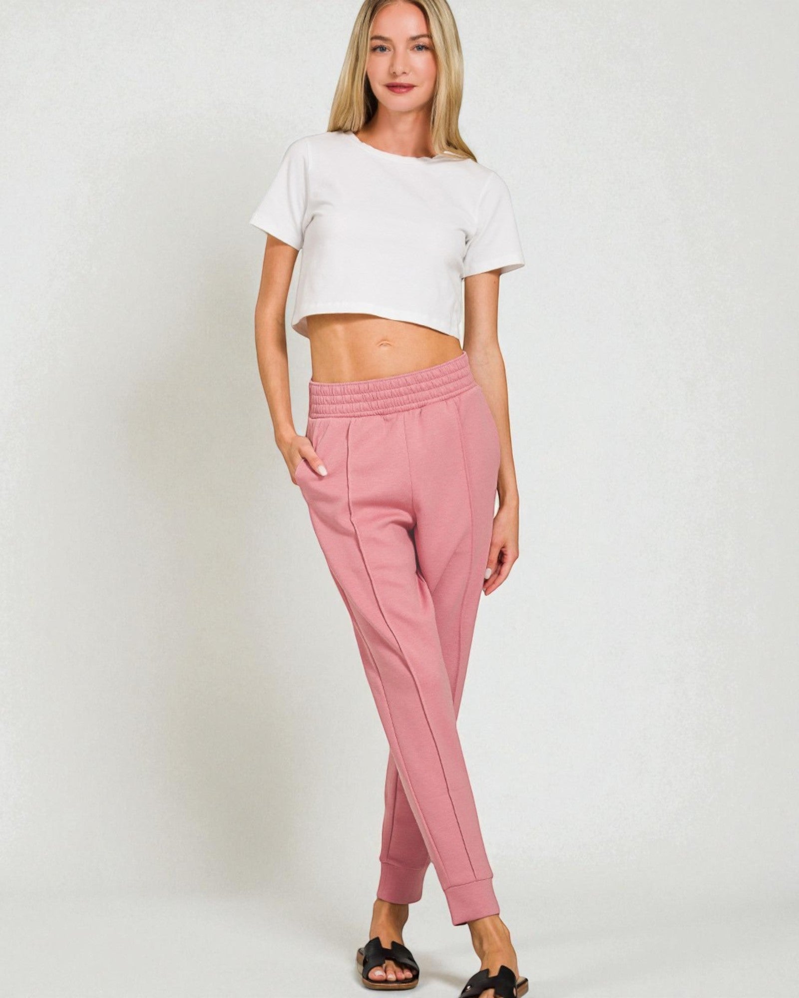 Woman wearing a white crop top and pink sweatpants on a plain background