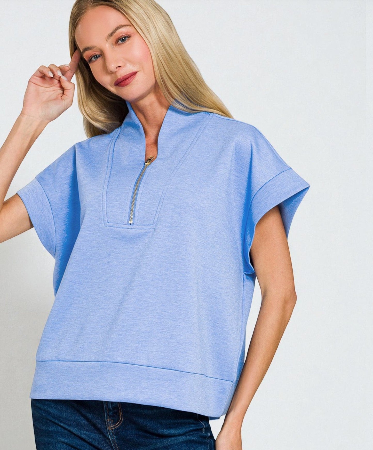 Woman wearing a light blue short-sleeve top with a zipper on a plain background