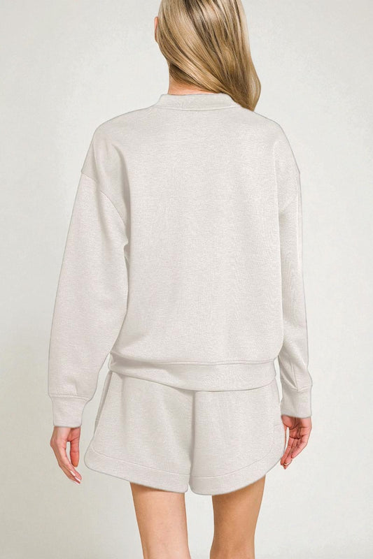 Person wearing a light gray sweatshirt and shorts set on a plain background