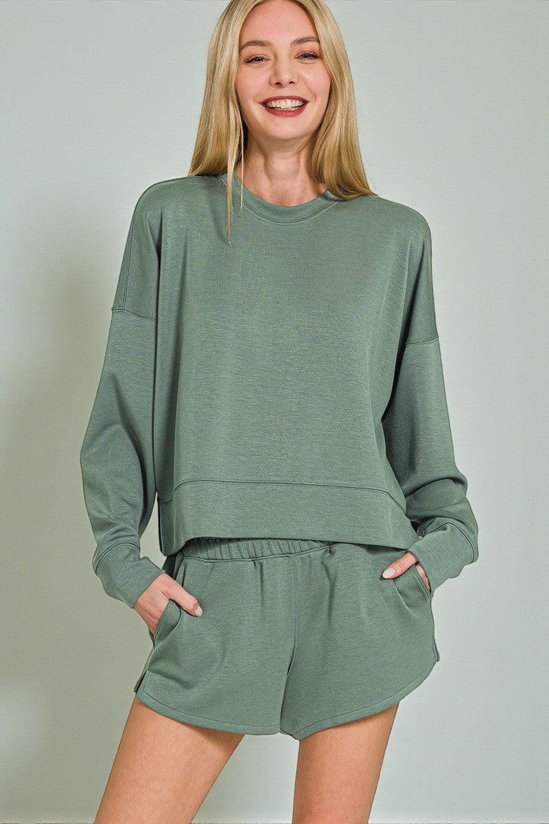 Woman wearing a green sweatshirt and shorts set against a plain background