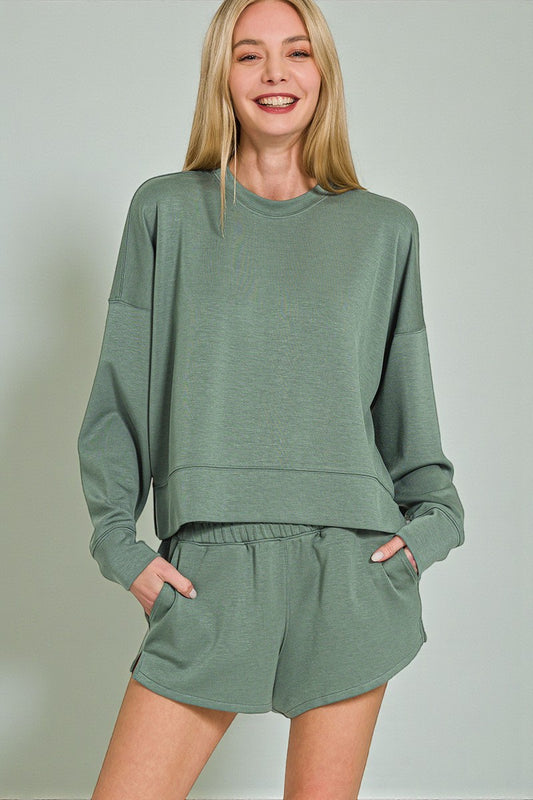 Woman wearing a green sweatshirt and shorts set against a plain background