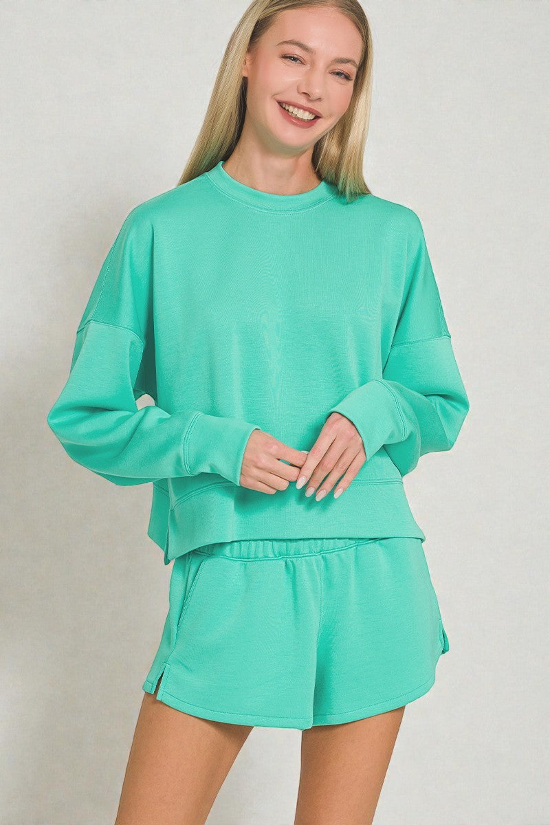 Woman wearing a teal sweatshirt and shorts set on a plain background