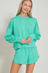 Woman wearing a teal sweatshirt and shorts set on a plain background