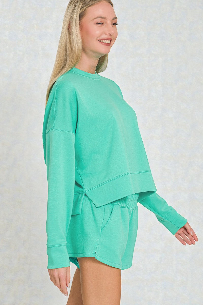 Woman wearing a mint green sweatshirt and shorts set on a light background