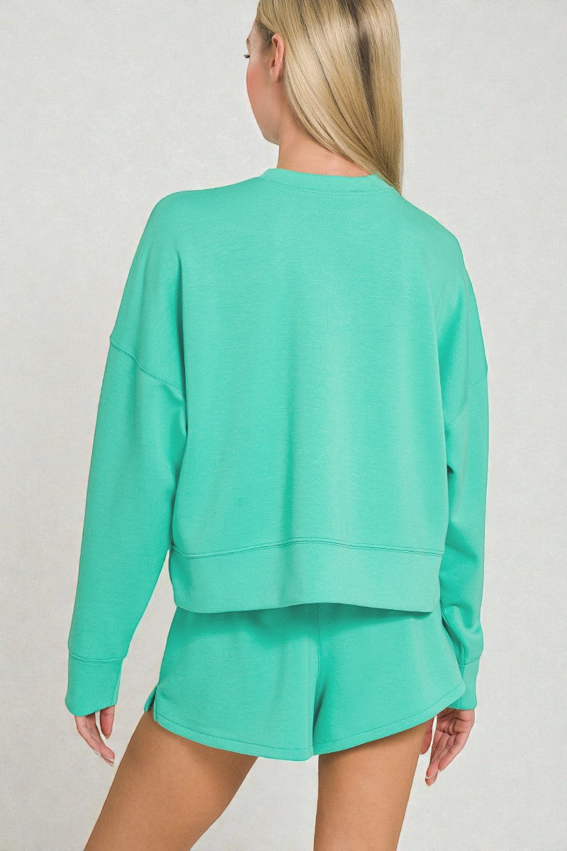 Person wearing a teal sweatshirt and shorts set on a plain background