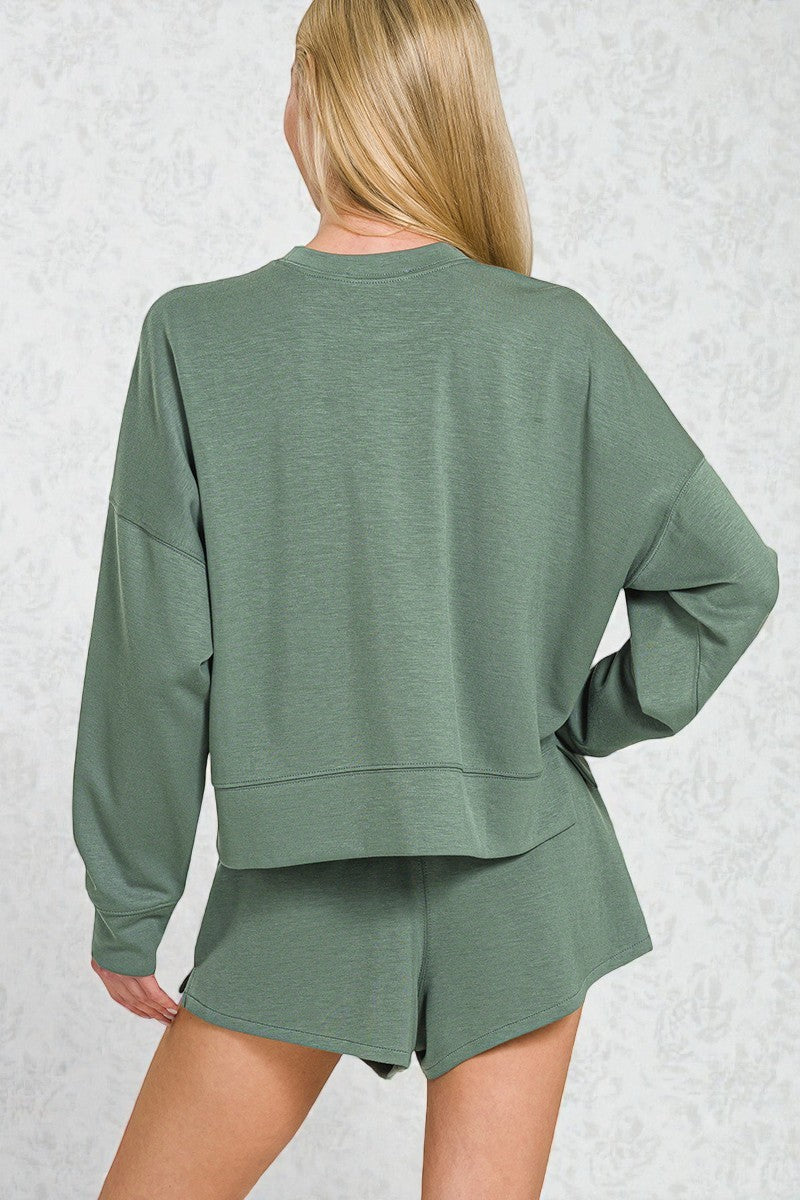 Person wearing a green long-sleeve top and shorts set on a light gray background