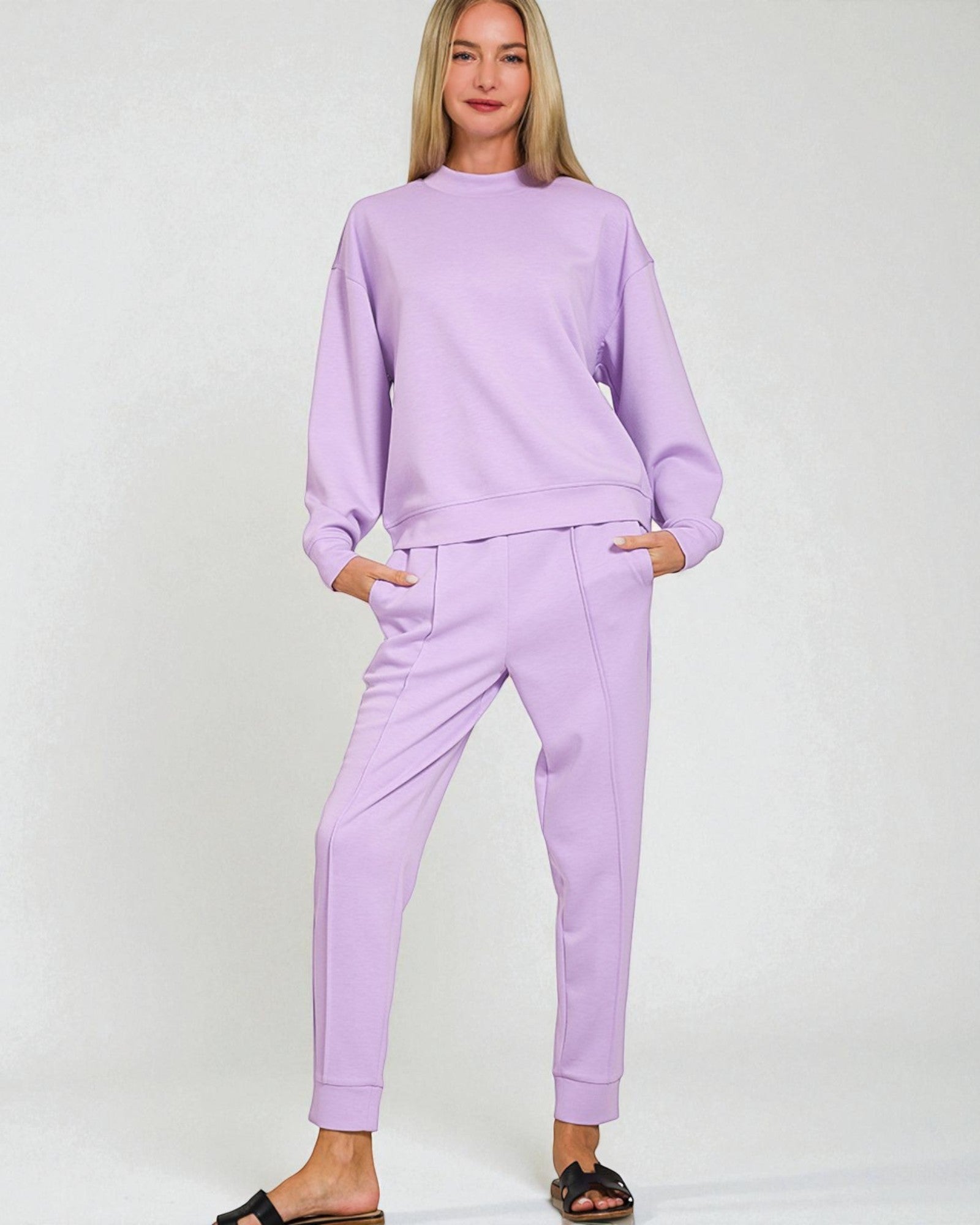 Woman wearing a matching lavender sweatshirt and pants set on a white background