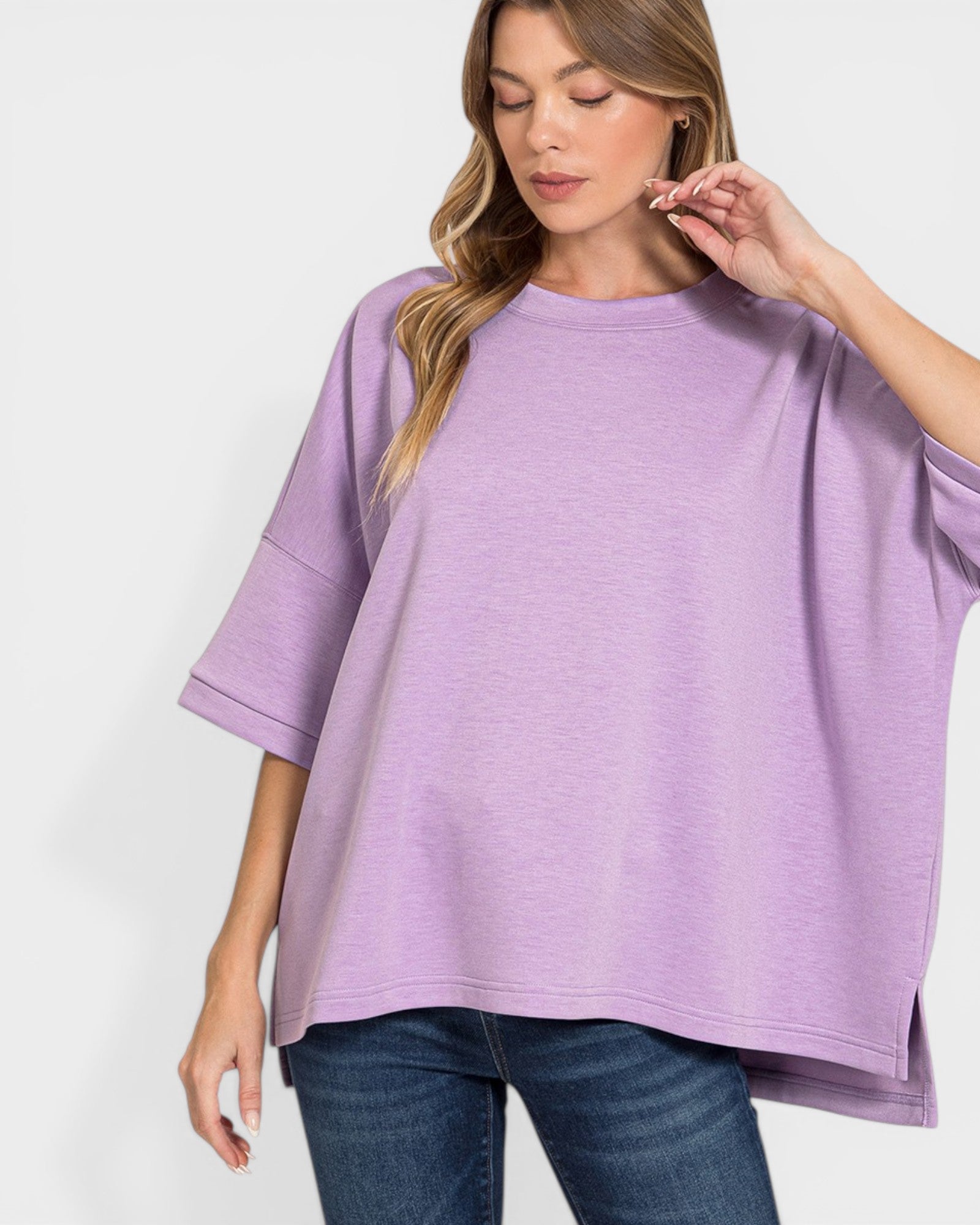 Woman wearing a purple oversized top and blue jeans on a white background