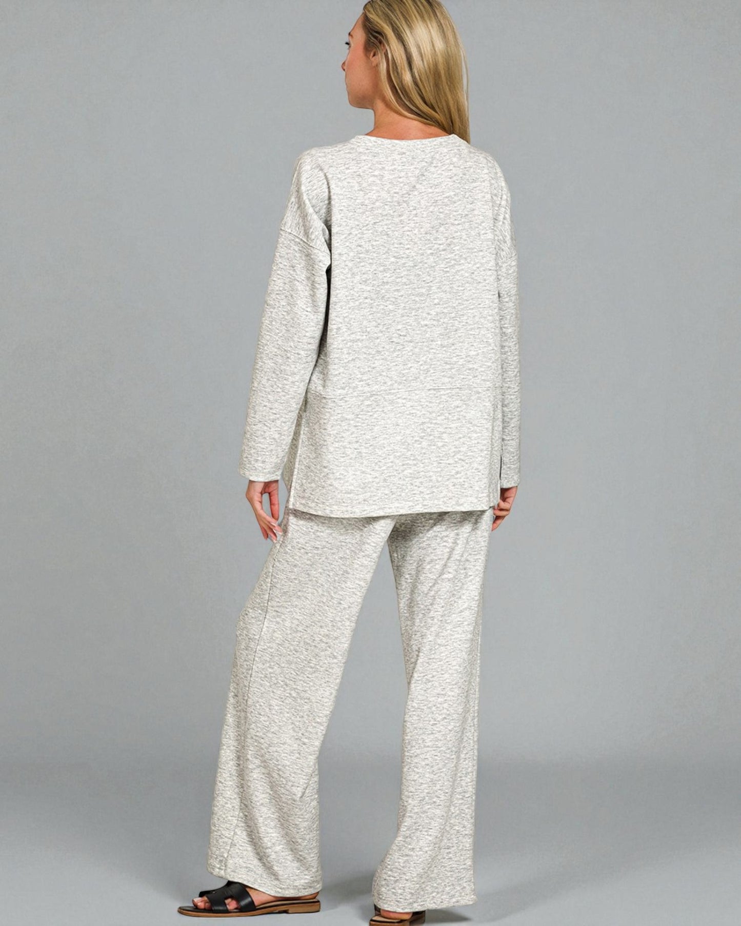 Woman wearing a light gray outfit with wide-leg pants on a plain background