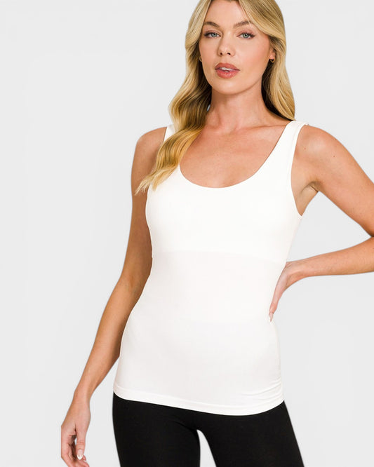 Woman wearing a white tank top and black leggings on a plain background