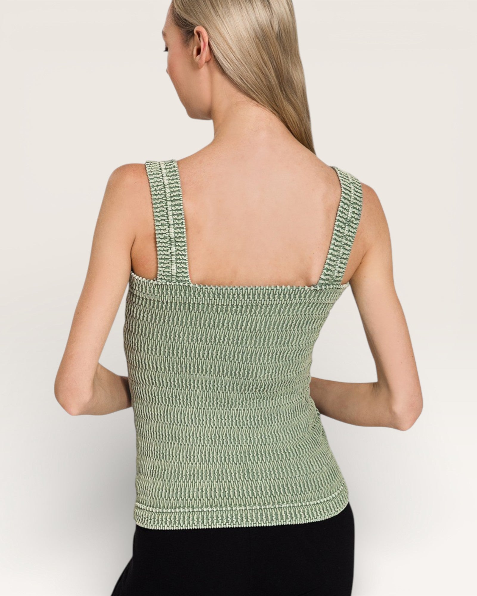 Woman wearing a green knitted tank top against a plain background
