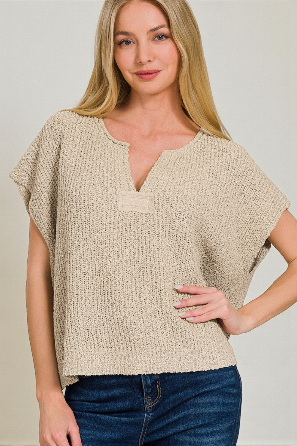 Woman wearing a beige knitted top with a plain background