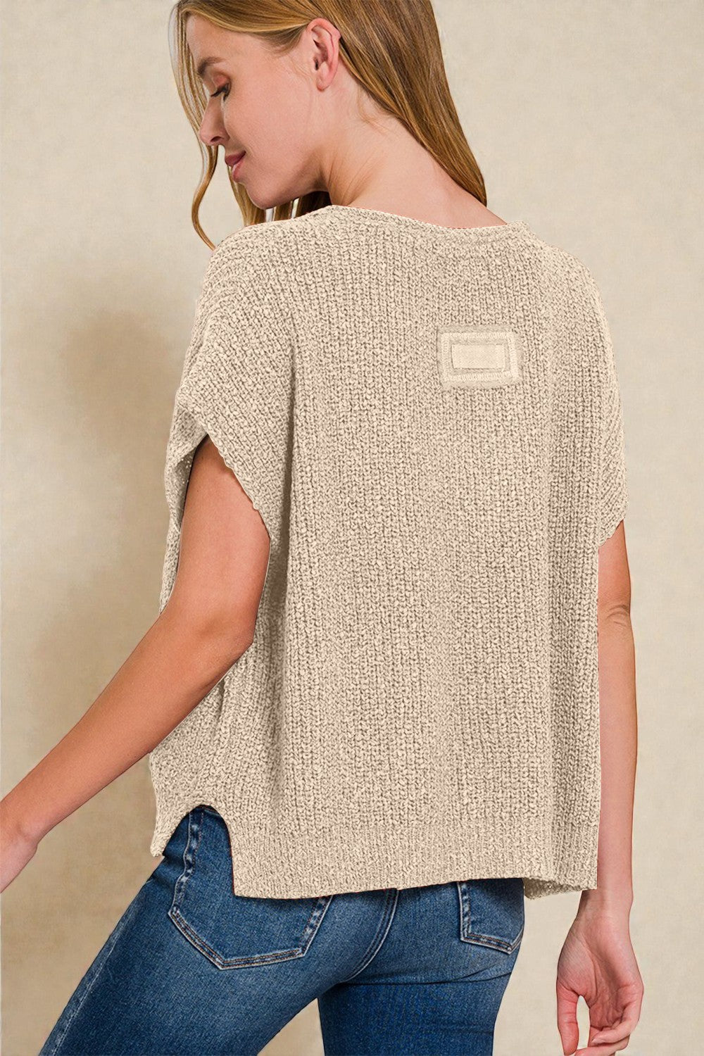 Woman wearing a beige textured top with a logo on a plain background