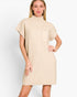 A woman modeling a beige ribbed knit mock-neck dress with short sleeves and a chest pocket, set against a plain light gray studio background.