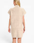 A woman shown from the back wearing a short-sleeve, ribbed knit dress in a light beige or cream color, set against a plain light gray studio background.
