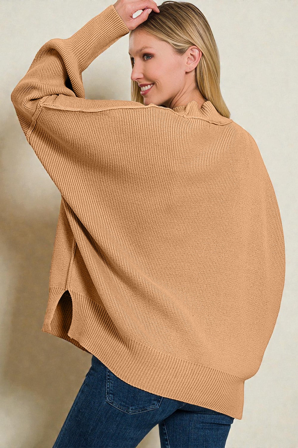 Woman wearing a tan sweater and blue jeans against a beige background