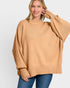A woman wearing a camel-colored ribbed knit sweater with balloon sleeves and blue jeans, photographed against a light gray studio background.