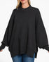 A woman wearing a black ribbed knit sweater with balloon sleeves and a mock neck, paired with blue jeans, against a plain white background.