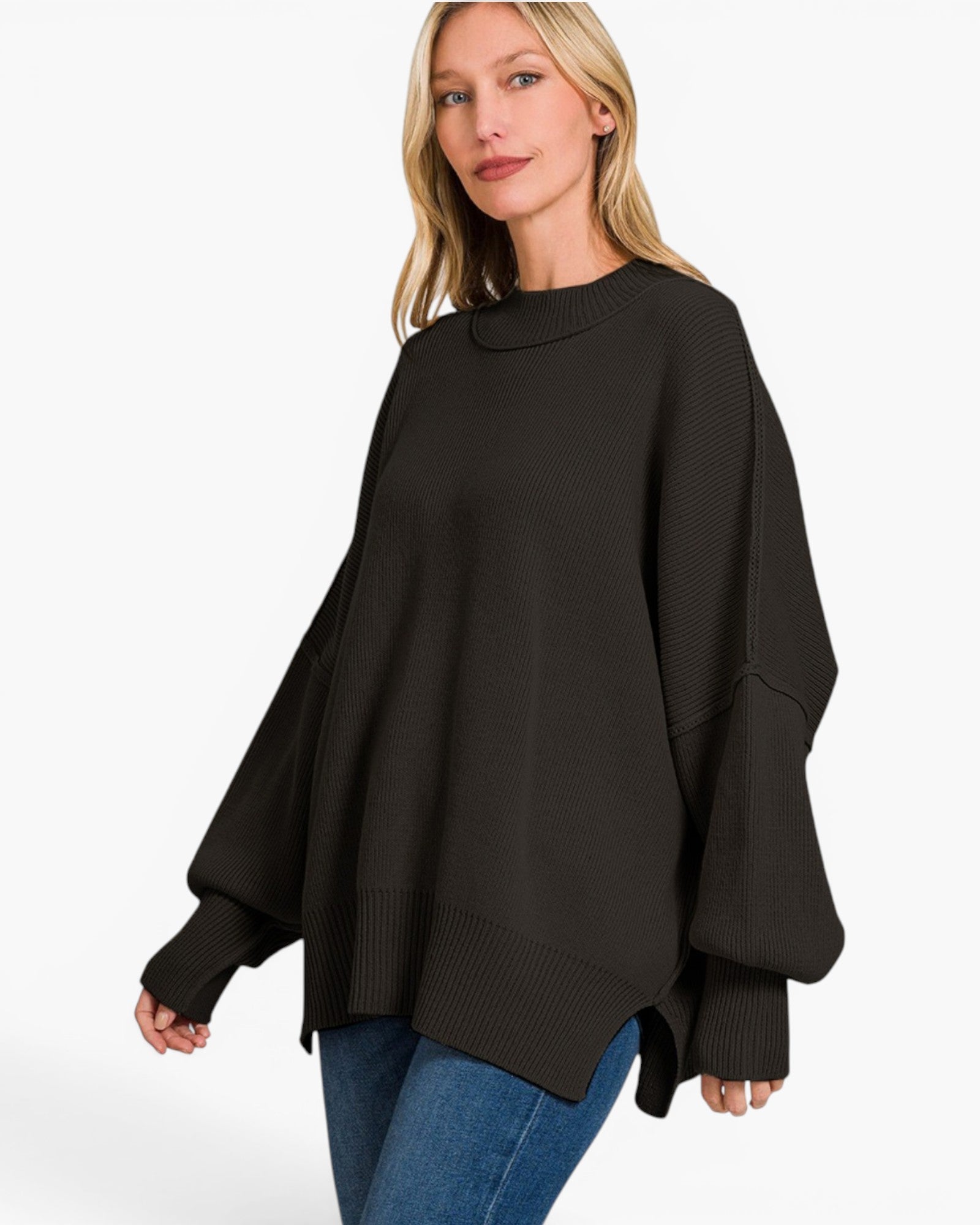 A woman wearing a black oversized knit sweater with wide balloon sleeves and blue jeans, photographed against a clean white studio background.