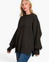 A woman wearing a black oversized knit sweater with wide balloon sleeves and blue jeans, photographed against a clean white studio background.