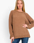A woman wearing a brown knit sweater with blue jeans, standing against a plain white studio background.