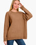 A woman wearing a brown knit crewneck sweater with raglan sleeves and a draped pocket detail on the upper sleeve, paired with blue jeans against a plain white background.