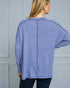 Woman wearing a blue long-sleeve top against a gray wall