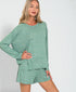 Woman wearing a green long-sleeve top and shorts set on a white background