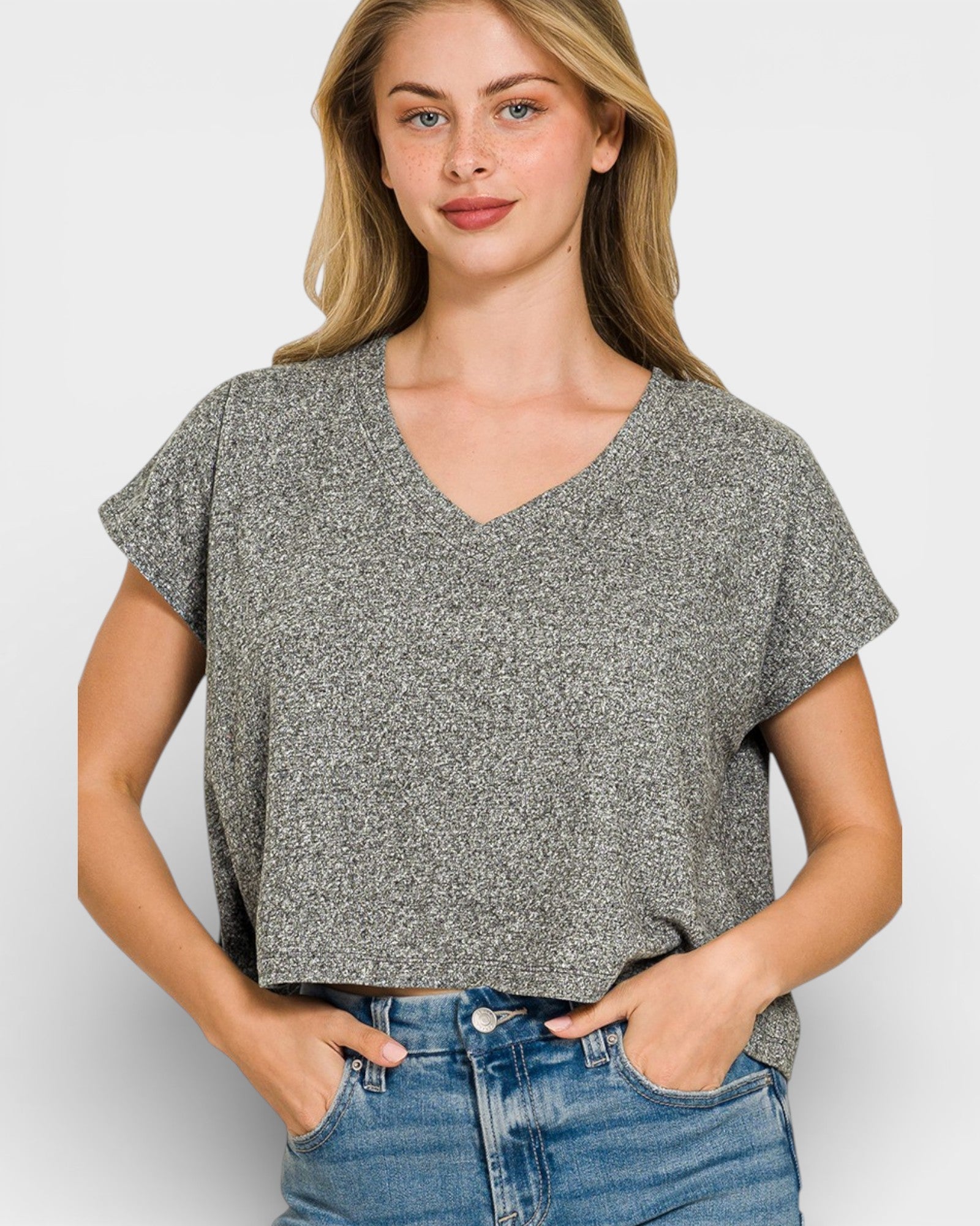 Woman wearing a gray patterned top and blue jeans on a white background