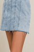 Light blue denim skirt with frayed hem on a beige background
