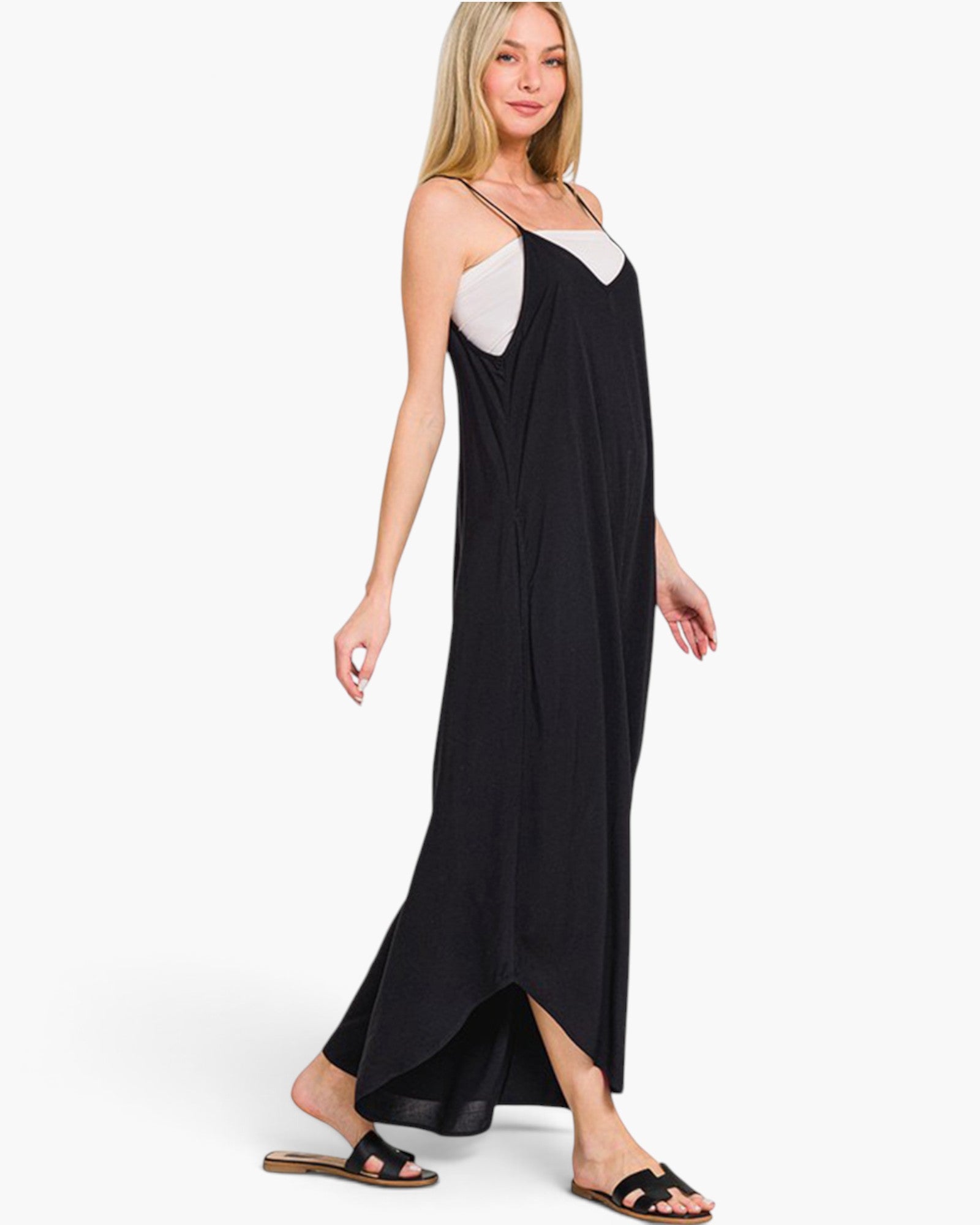A woman modeling a black wide leg jumpsuit, paired with black slide sandals against a plain white studio background.