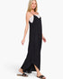 A woman modeling a black wide leg jumpsuit, paired with black slide sandals against a plain white studio background.