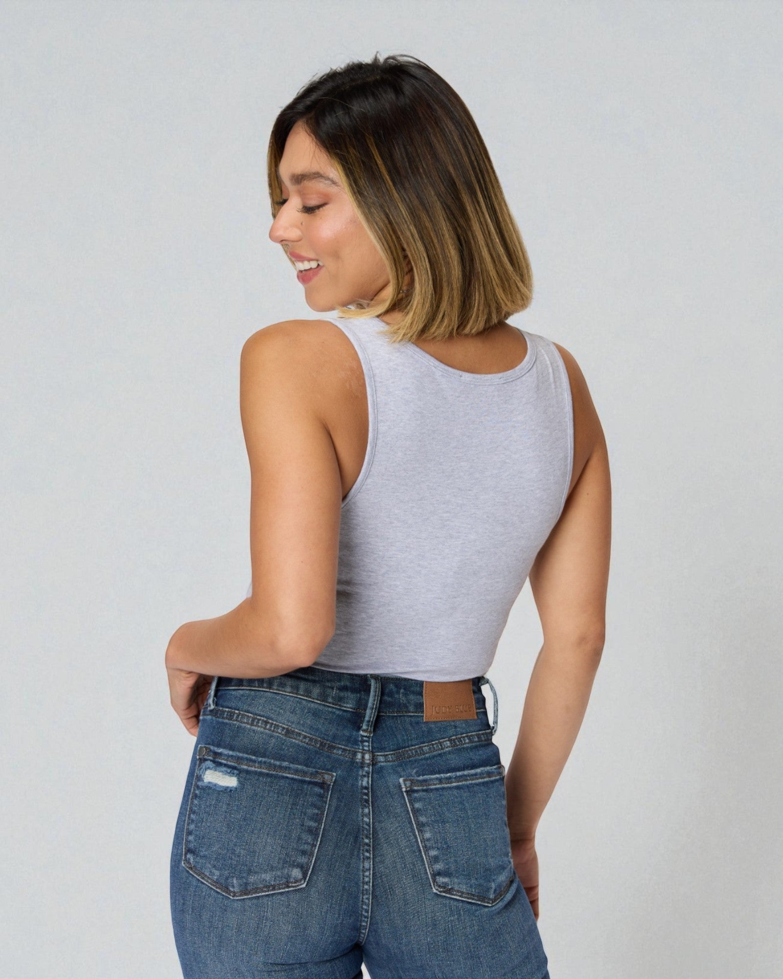 Woman wearing a gray tank top and blue jeans against a white background