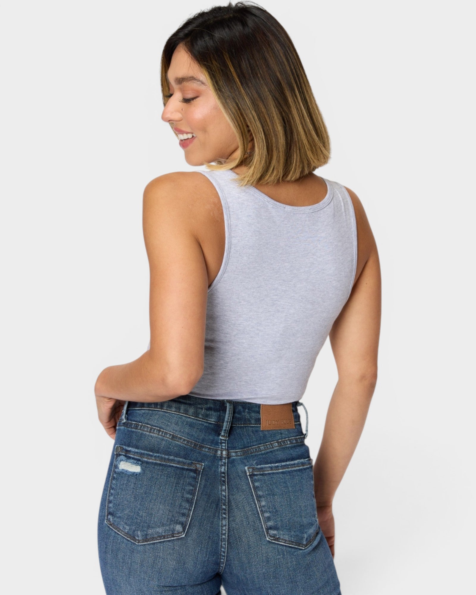 Woman wearing a gray tank top and blue jeans on a white background