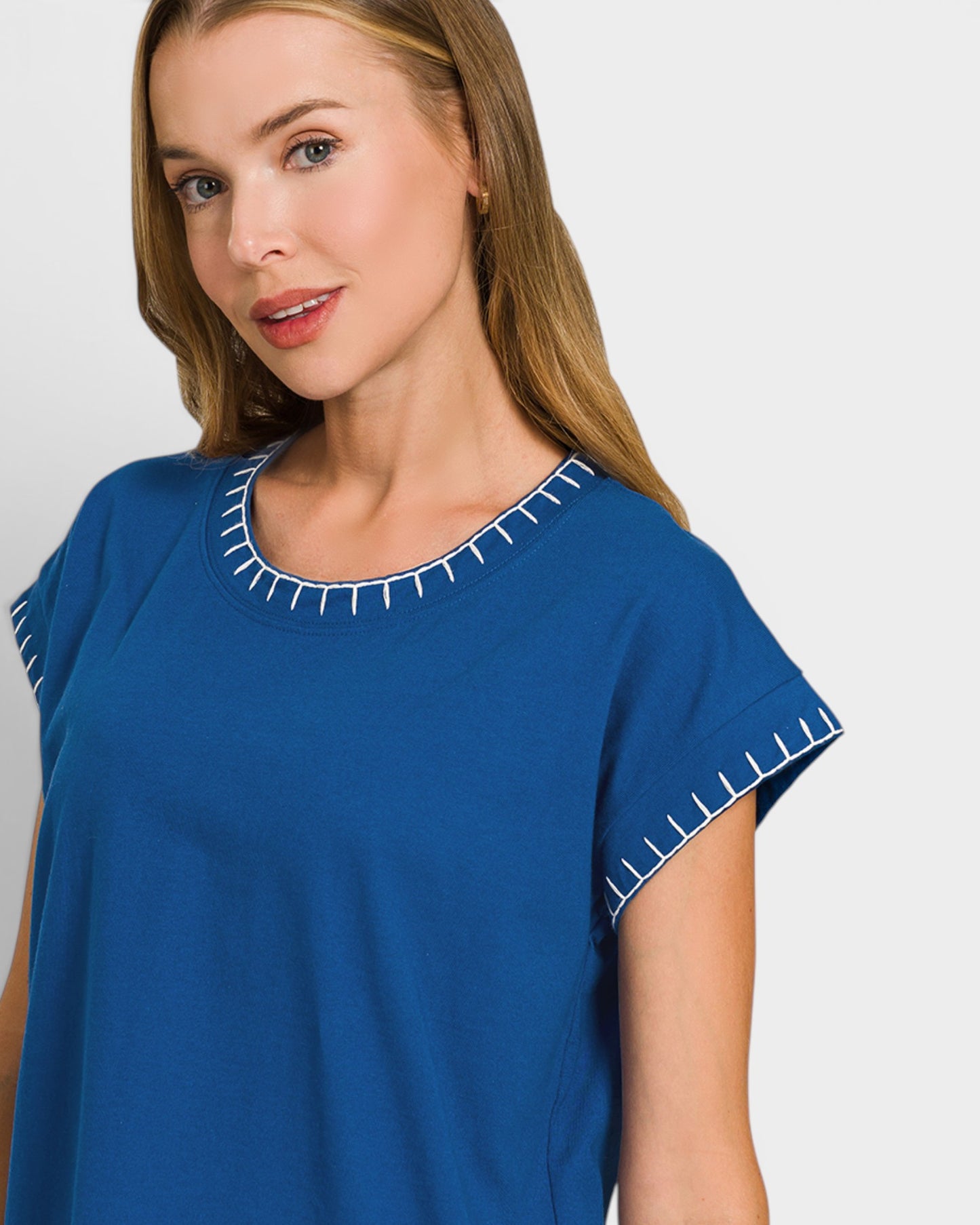 Woman wearing a blue top with white trim on a plain background