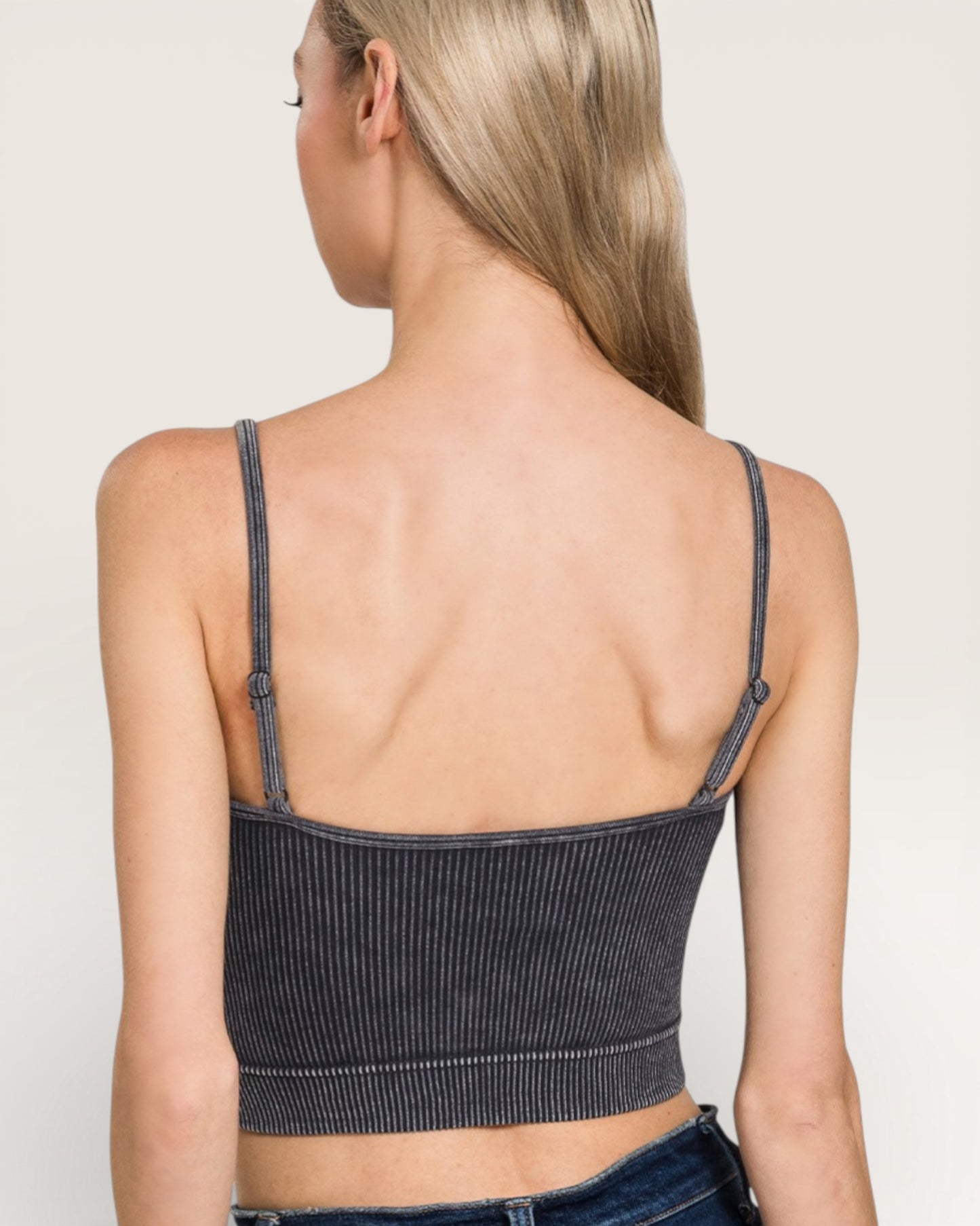 Person wearing a black ribbed tank top with thin straps on a plain background