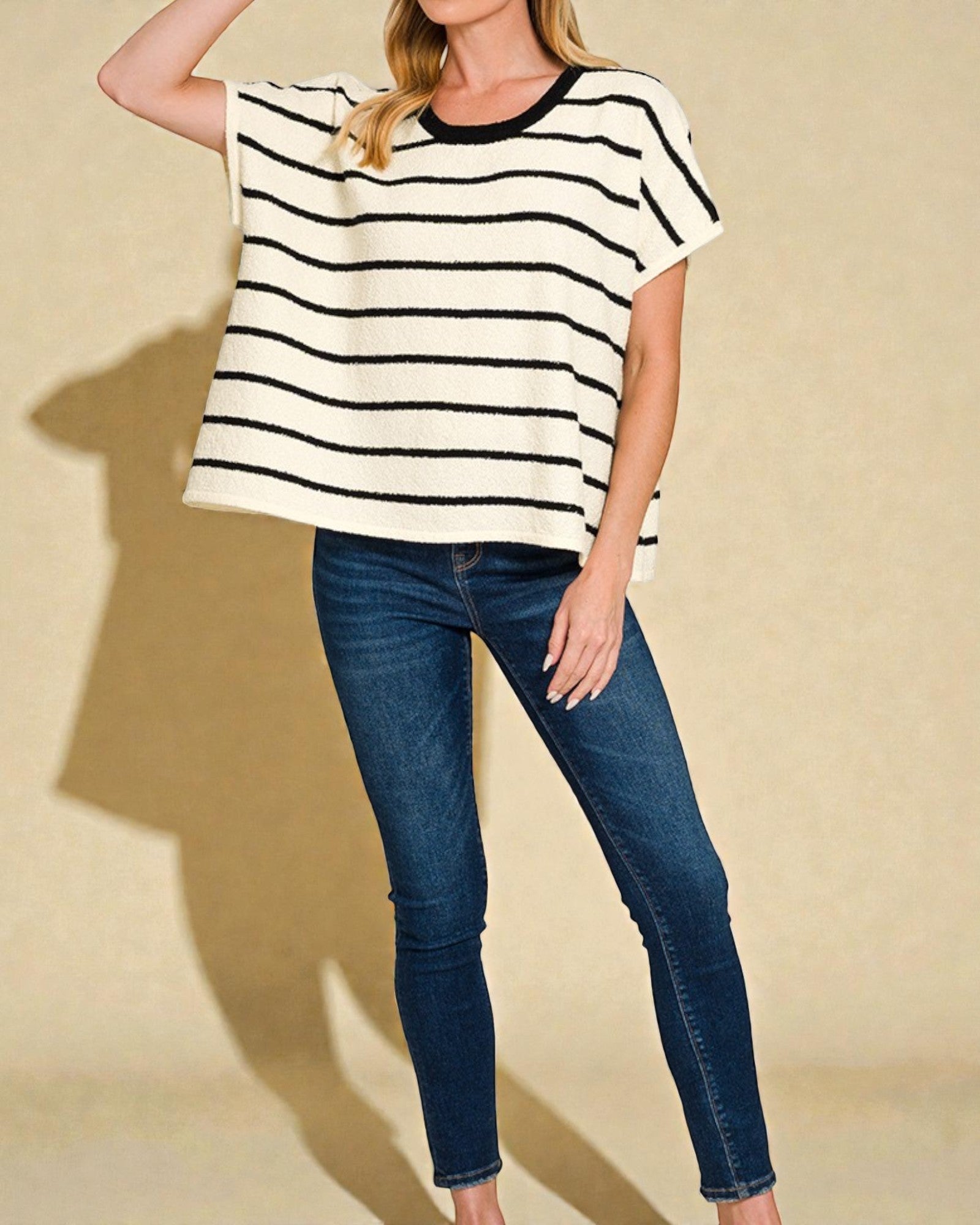 Person wearing a black and white striped shirt and blue jeans on a beige background