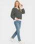 Woman wearing a black and white striped sweater with a white shirt underneath, blue jeans, and white sneakers on a light gray background.