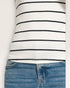 Close-up of a person wearing a white long-sleeve shirt with black stripes and blue jeans on a light gray background.