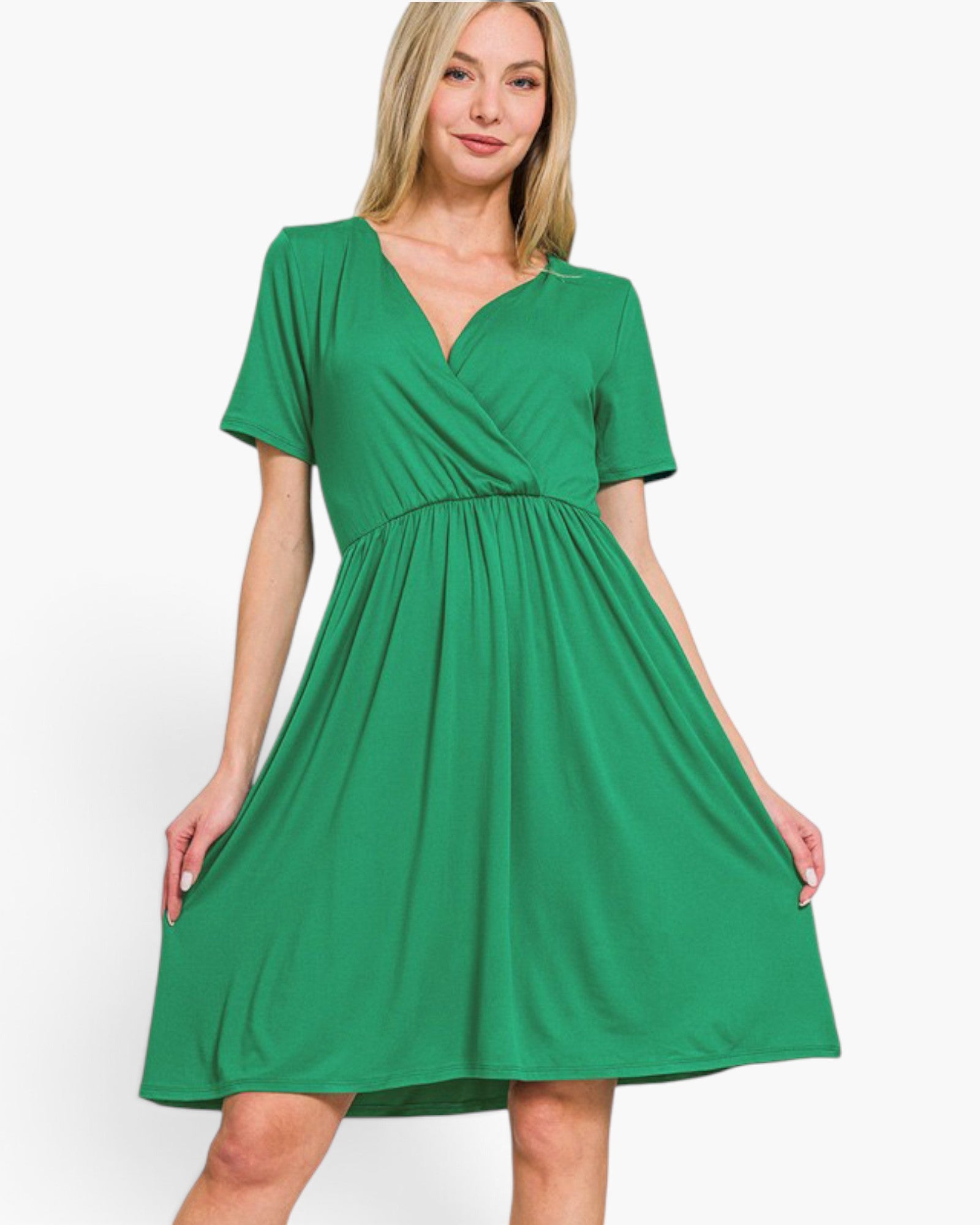 A woman modeling a bright green short-sleeve wrap-style dress with a gathered waist and flared skirt, photographed against a plain light gray studio background.