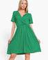 A woman modeling a bright green short-sleeve wrap-style dress with a gathered waist and flared skirt, photographed against a plain light gray studio background.
